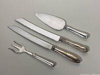 Four sterling silver serving utensils laid on neutral surface, showing full handles and blades