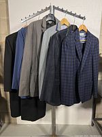 Five men's jackets hanging on rack showing variety of colors and styles including dark, pinstripe, gray, charcoal, and blue checked patterns.