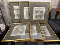 Group of six gold-tone framed engravings with gray mats arranged on a table