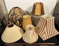 View of all seven assorted vintage lampshades together showing variety in size, shape, pattern and material.