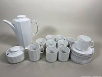 Full set arranged showing coffee pot, sugar bowl with lid, creamer, mugs stacked on saucers, and loose mugs.
