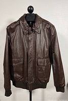 Front view of the brown leather bomber jacket with collar, flap pockets, and zippered front covered by flap.
