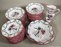 Stacks of various hand painted ceramic plates with floral designs in red, blue, and green, including dinner and luncheon plates, plus a small pitcher and creamer.