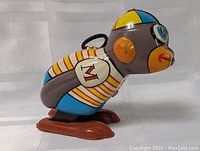 Side view of colorful vintage wind-up monkey toy with striped shirt, blue and yellow cap, and plastic feet.