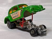 Photo showing front and underside of green 1972 Matchbox Lesney Dragon Wheels Volkswagen toy car with lifted body revealing chrome engine and chassis details, black tires with silver hubs.