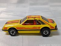 Side view of the die cast Hot Wheels Mustang car showing yellow body with flame decals and red interior.