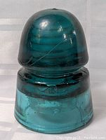 Front view of the dome-shaped aqua glass insulator with smooth rounded top and concentric ridges inside the glass.