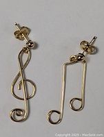 Pair of gold plated earrings shaped as treble clef musical notes, showing front and side views.