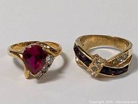 Pair of gold plated vintage rings, one with large pear-shaped deep red stone and clear stones, second with dark red rectangular stones and clear stone accents