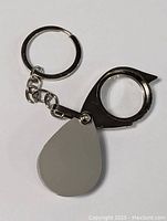 Closed jeweler's loupe keychain showing teardrop-shaped metal cover and key ring attachment.