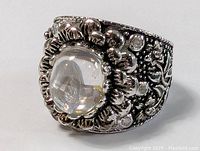 Close-up image showing the front and side profile of the silver plated ring with a round quartz cabochon stone set in the center and floral decorative metalwork on the band.