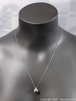 Silver necklace displayed on black mannequin with a crown pendant encrusted with small stones, showing front view of pendant and part of chain.