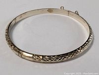 Full view of the sterling silver carved bangle bracelet showing the oval shape and clasp with missing safety chain attachments.