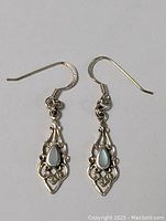Photo showing both earrings with intricate filigree and blue teardrop stone detail.