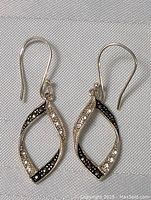 Front facing photo of the pair of sterling silver twisted loop dangle earrings with marcasite stones on white fabric background.