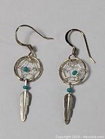 Pair of sterling silver dreamcatcher earrings with turquoise beads and feather pendants, displayed on white background, showing front and side view.