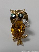 Front view of vintage owl brooch pin highlighting the faceted amber oval body gem, black and green eyes, and white marquise wing stone.