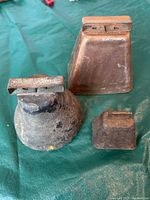 Three antique primitive metal bells of different sizes and shapes placed on a green cloth surface