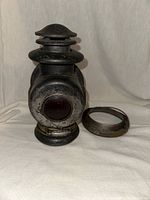 Front view of the antique railroad lantern, showing round red glass lens and metal ventilation cap.