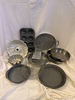 Full display of baking and cooking pans and tools including muffin pan, bundt pans, grater, wire basket, pizza pan, frying pans, and round baking pans.
