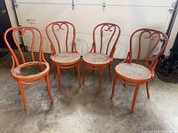 Set of four orange bentwood chairs arranged in front of a garage door on a concrete floor, showing overall condition and paint color.