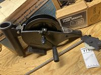Cannon black metal downrigger reel with attached rod holder and hand crank, placed on wooden surface.