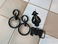 Four cast iron hooks and hanger items shown on tile floor, including two ring hooks, decorative hanger, and mounting bracket.