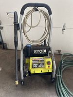 Full front view of Ryobi electric pressure washer showing handle, garden hose, spray wand, and brand/logo.