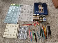 Full lot overview showing stencils, paint palettes, paint jars, tubes, and many paintbrushes spread out on floor.