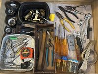 Photo showing organized assortment of hand tools including screwdrivers, adjustable wrenches, pliers, wire cutters, rolls of tape, and jars with fasteners.