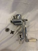 Disassembled view showing main grinder body with clamp and crank handle plus two extra grinding blades (star and cross shaped).