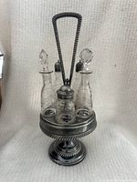 Full view of Victorian silver plated cruet set on raised pedestal stand with twisted rope detail and tall handle. Shows five glass bottles arranged on the stand.