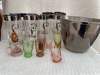 Front view of the set showing 8 tall glasses with silver rims and L initials, multicolored shot glasses, novelty corkscrew in small pink glass cup, and stainless steel ice bucket.