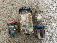 Four glass jars filled with various vintage buttons in assorted colors and sizes on carpet background.