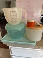 Various vintage storage containers stacked, showing different sizes and colors including light blue, orange, and white with beige lid