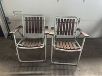 Front view of two vintage folding chairs with aluminum metal frames and wooden slats on seat, back, and squared wooden arms.