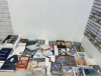 Wide shot showing entire lot of Blu-ray discs, DVDs and books arranged on a table against a white wall and brick background.