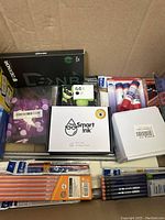 Overview of the stationery box showing multiple ink cartridges, glue sticks, pencils, and office supplies.
