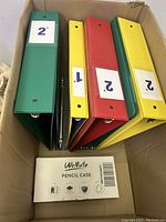 Five ring binders arranged inside cardboard box with green, red, and yellow colors