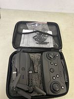 Closed foam-padded carrying case with foldable drone, extra propellers and user manual visible in mesh pocket.