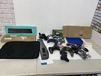 All items arranged on a table showing various electronics including controllers, keyboard box, and cables.