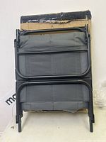 Folded lounge chair resting on a cardboard box, showing black metal frame and grey fabric seat.