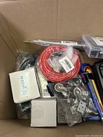 Box contents showing various items including red cable, Moen box, hardware parts, hex keys, battery charger, and organizer box.