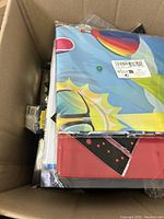 Box filled with decorative banners, one showing sun and rainbow graphics, some still in plastic packaging.
