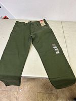 Full length photo of olive green Levi's chinos laid flat on white table, showing tapered leg jeans with no signs of wear and tagged with original labels.
