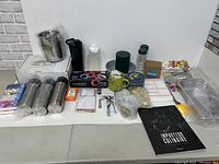 Wide view of assorted kitchen and household items including cups, containers, utensils, and paper notepads spread out on a table.