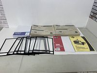 Contents of lot laid out showing black plastic sleeves, notebooks, lined paper, and two boxes of Kraft envelopes