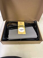 Unassembled Veehoo slope elevated dog bed components in box, showing black metal frame pieces and gray mesh sleep surface.