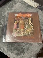 Front cover of Aerosmith "Toys in the Attic" vinyl record showing colorful attic-themed cartoon artwork with the band's logo.