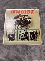 Front cover of Beatles 65 vinyl album showing four band members sitting and holding umbrellas.